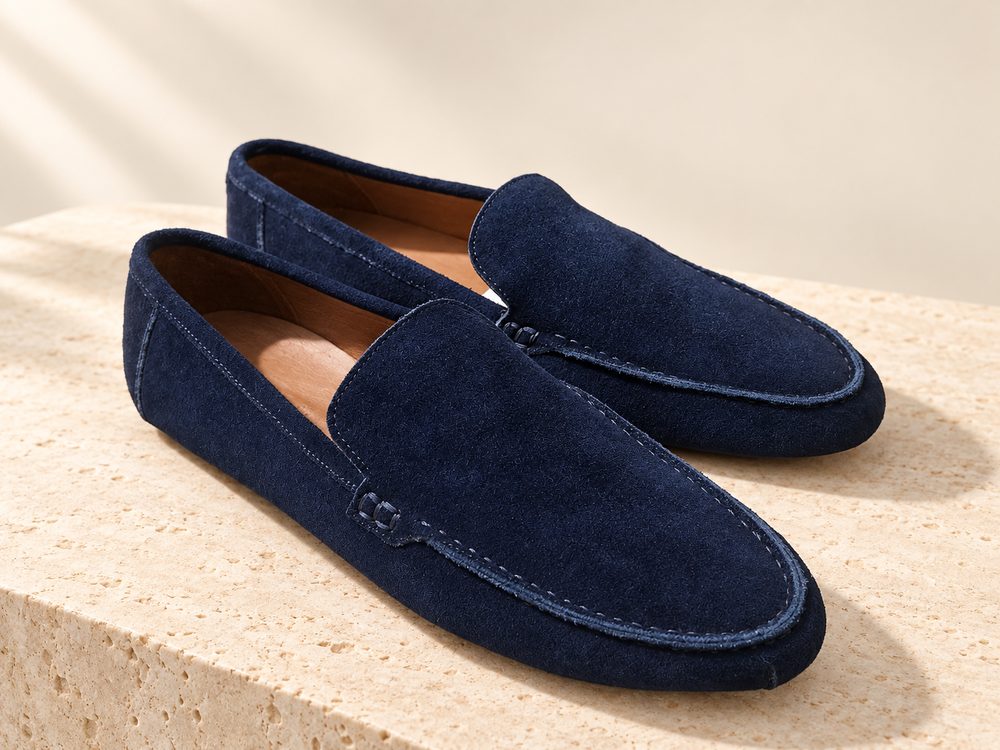 Visuel d'ambiance généré par IA : une paire de mocassins en daim bleu marine sur un bloc de pierre claire, semelle marine