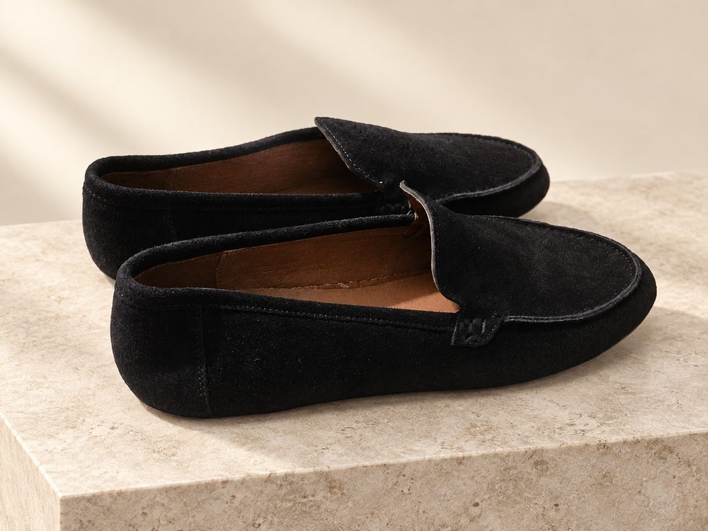 Visuel d'ambiance généré par IA : une paire de mocassins en daim noir sur un bloc de pierre claire, semelle noire